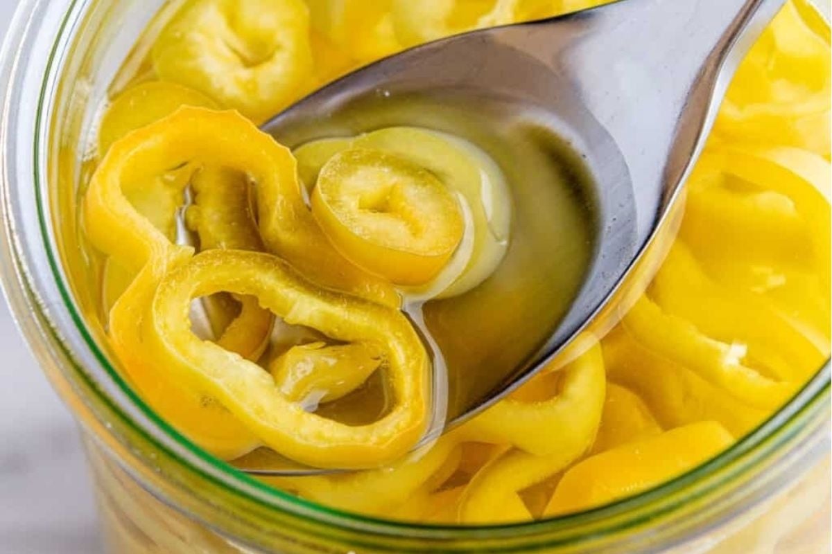 Sliced yellow banana peppers pickled in brine, with a spoon resting inside the jar.