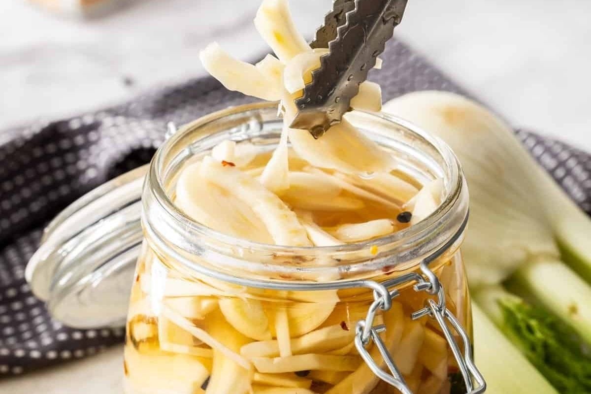A jar of pickled strings of cheese being served with tongs, a unique addition to pickled recipes.