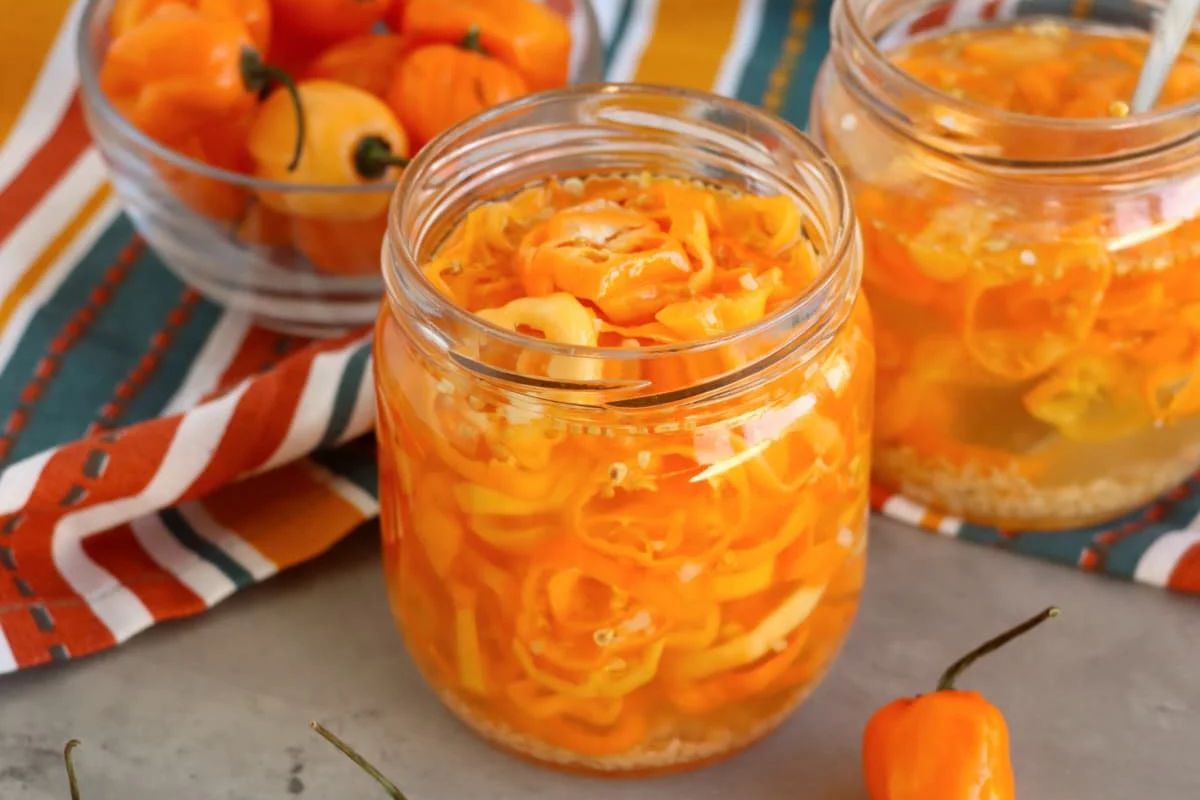 Two jars of pickled recipes with whole habanero peppers on a striped cloth.