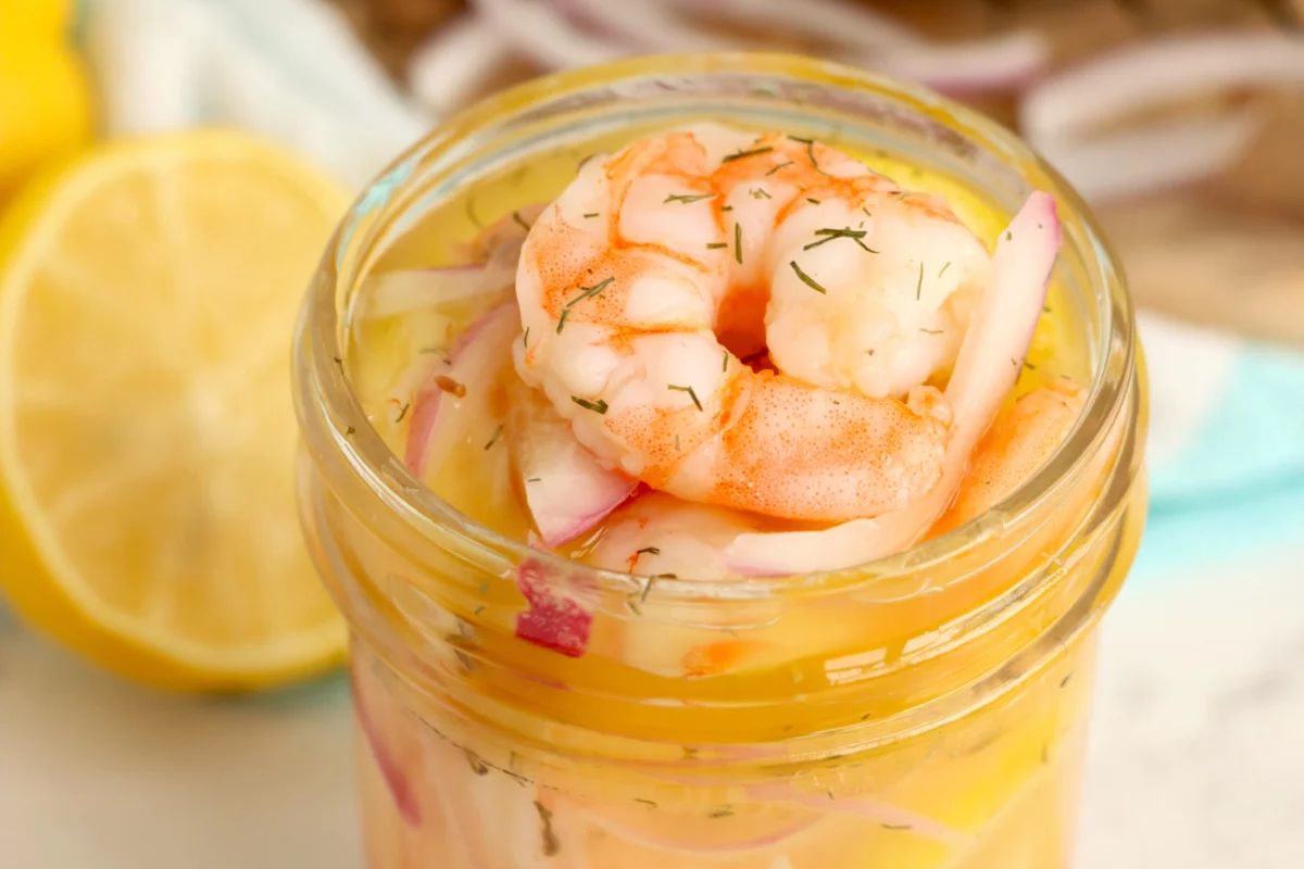 A jar of pickled shrimp garnished with dill, accompanied by a slice of lemon, serves as a delightful addition to pickled recipes.