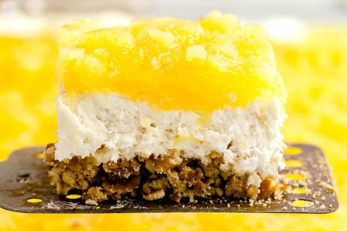 A slice of Easter dessert with a crumbly base, white cream center, and yellow topping on a spatula.