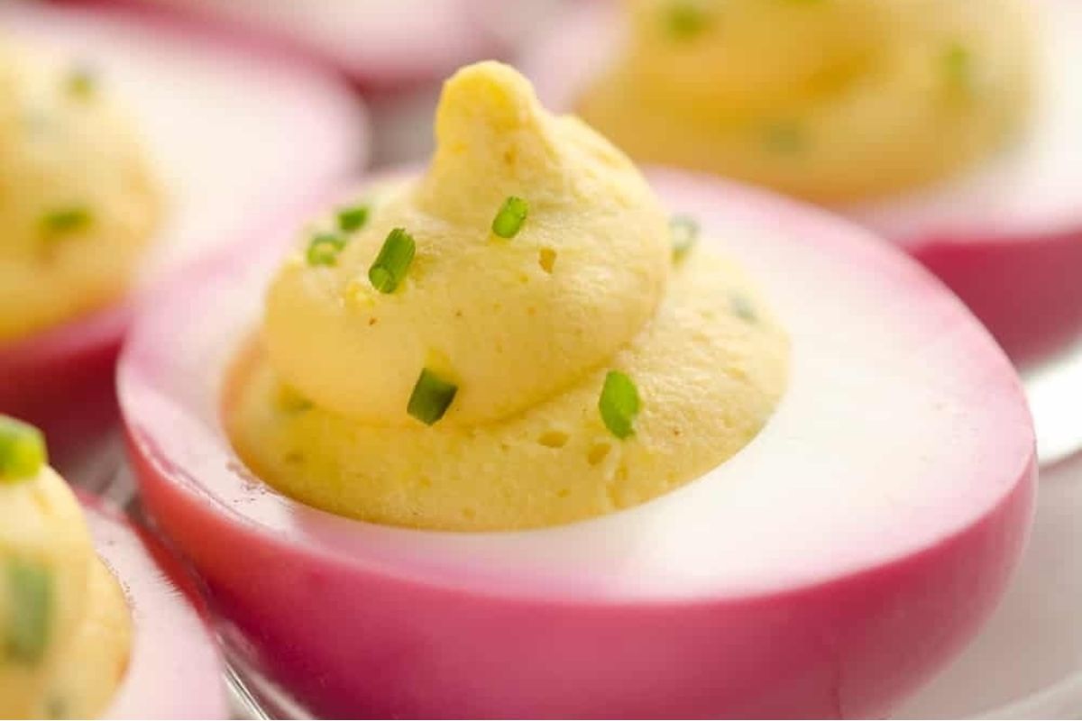 Deviled eggs garnished with pickled chives on a plate.