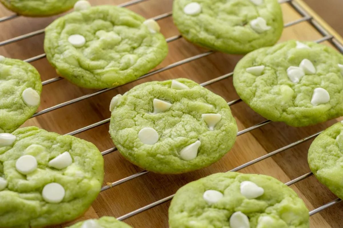 Freshly baked green Easter cookies with white chocolate chips cooling on a wire rack.