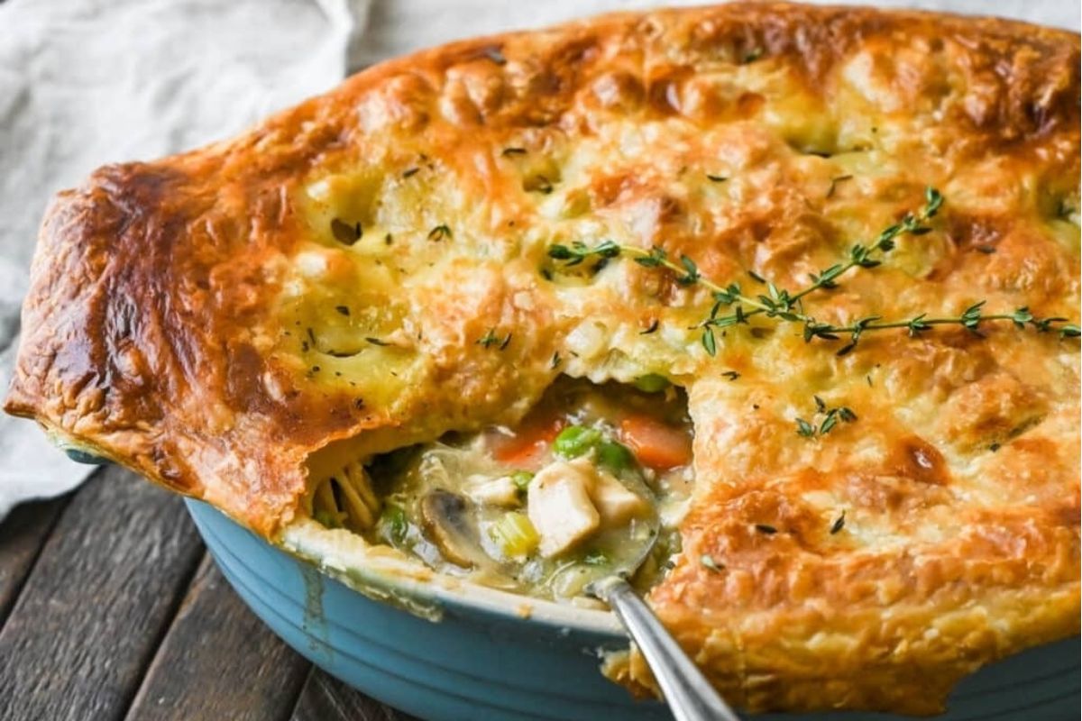 Golden-brown pot pie with flaky crust, filled with pizza flavored vegetables and chicken, garnished with fresh thyme.
