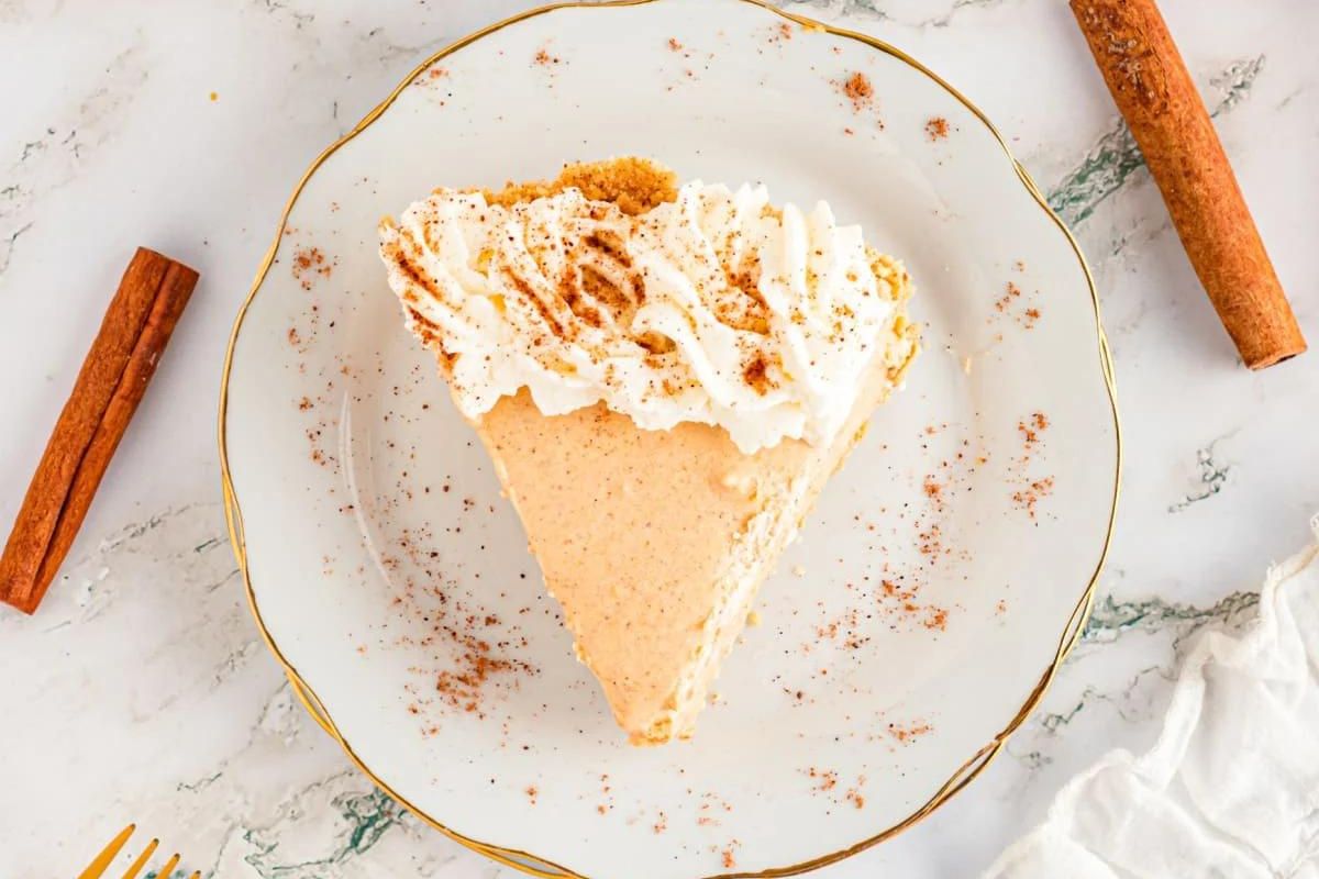 A slice of pumpkin pie recipes with whipped cream and a sprinkle of cinnamon on top, served on a plate with gold trim.