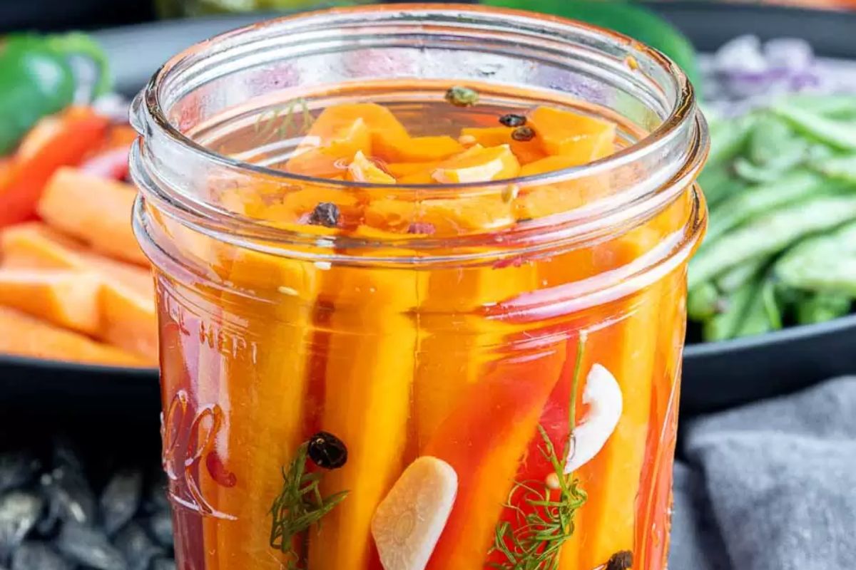 A jar of pickled carrots with spices, herbs, and recipes.