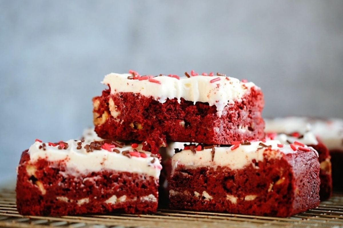 Stack of red velvet cookie recipes with cream cheese frosting and sprinkles on a cooling rack.