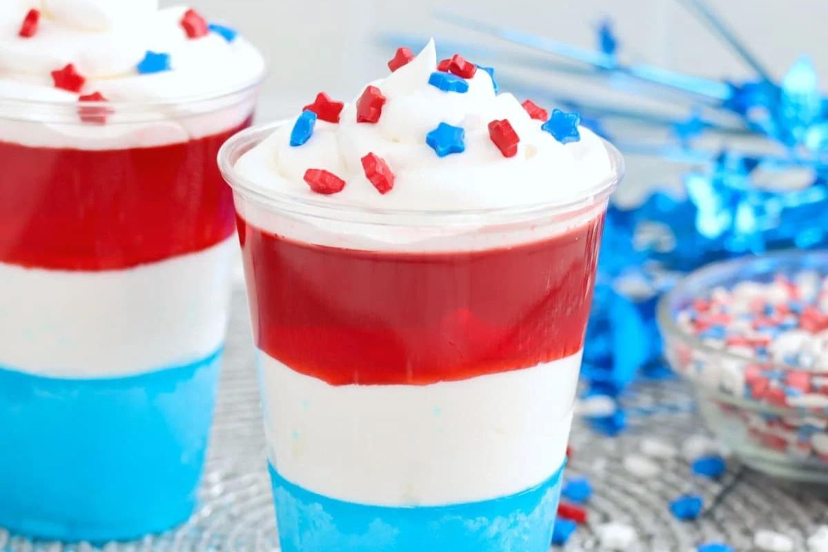 Layered red, white, and blue Jello desserts topped with whipped cream and sprinkled with star-shaped candies.