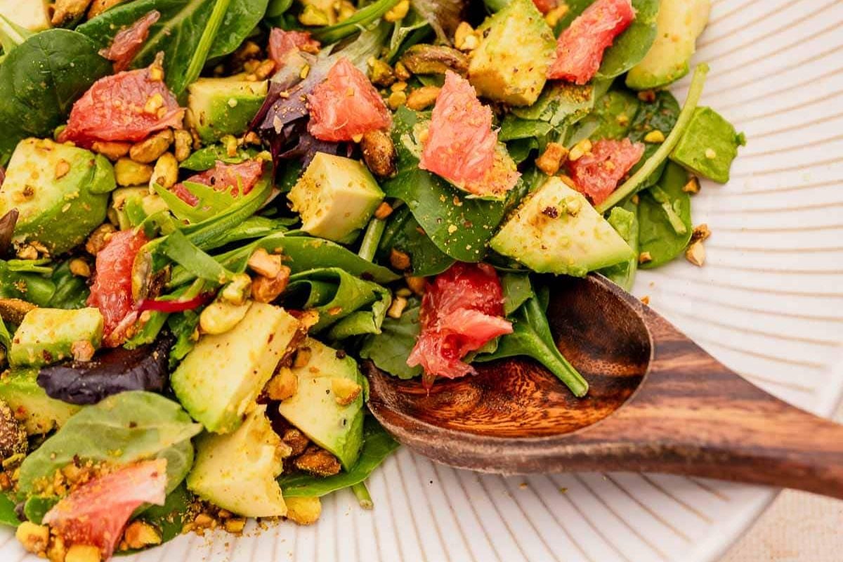 Close-up of a fresh avocado and grapefruit salad with greens and nuts, served as an Easter appetizer with a wooden spoon.