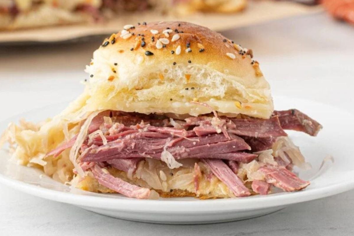 A corned beef and sauerkraut slider with a seeded bun on a plate.