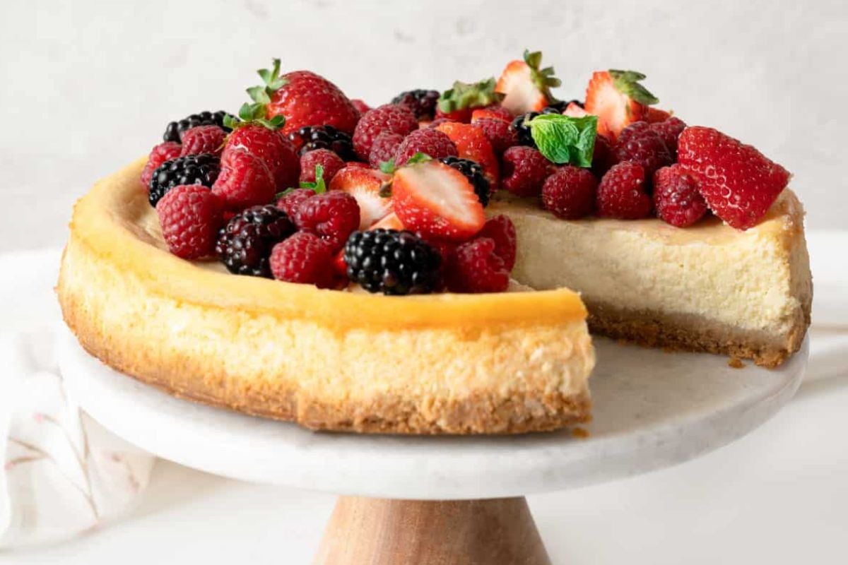 An Easter cheesecake topped with strawberries, raspberries, and blackberries on a wooden cake stand.