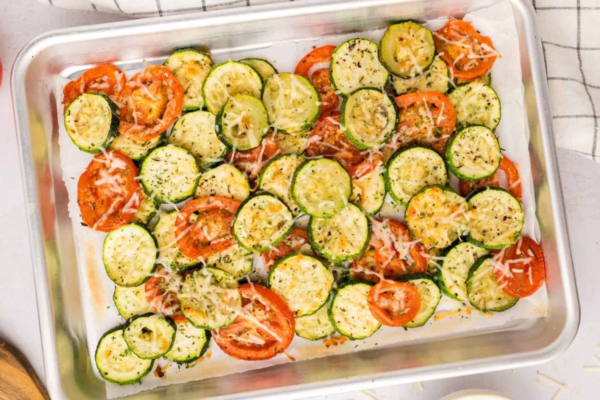 Sliced tomatoes and zucchinis seasoned and arranged on a baking sheet for roasting, perfect as Easter sides.