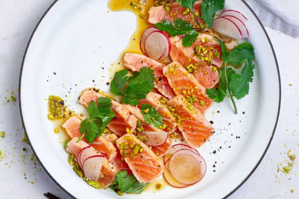 An Easter appetizer: a plate of salmon carpaccio garnished with radish slices, herbs, and a drizzle of sauce.