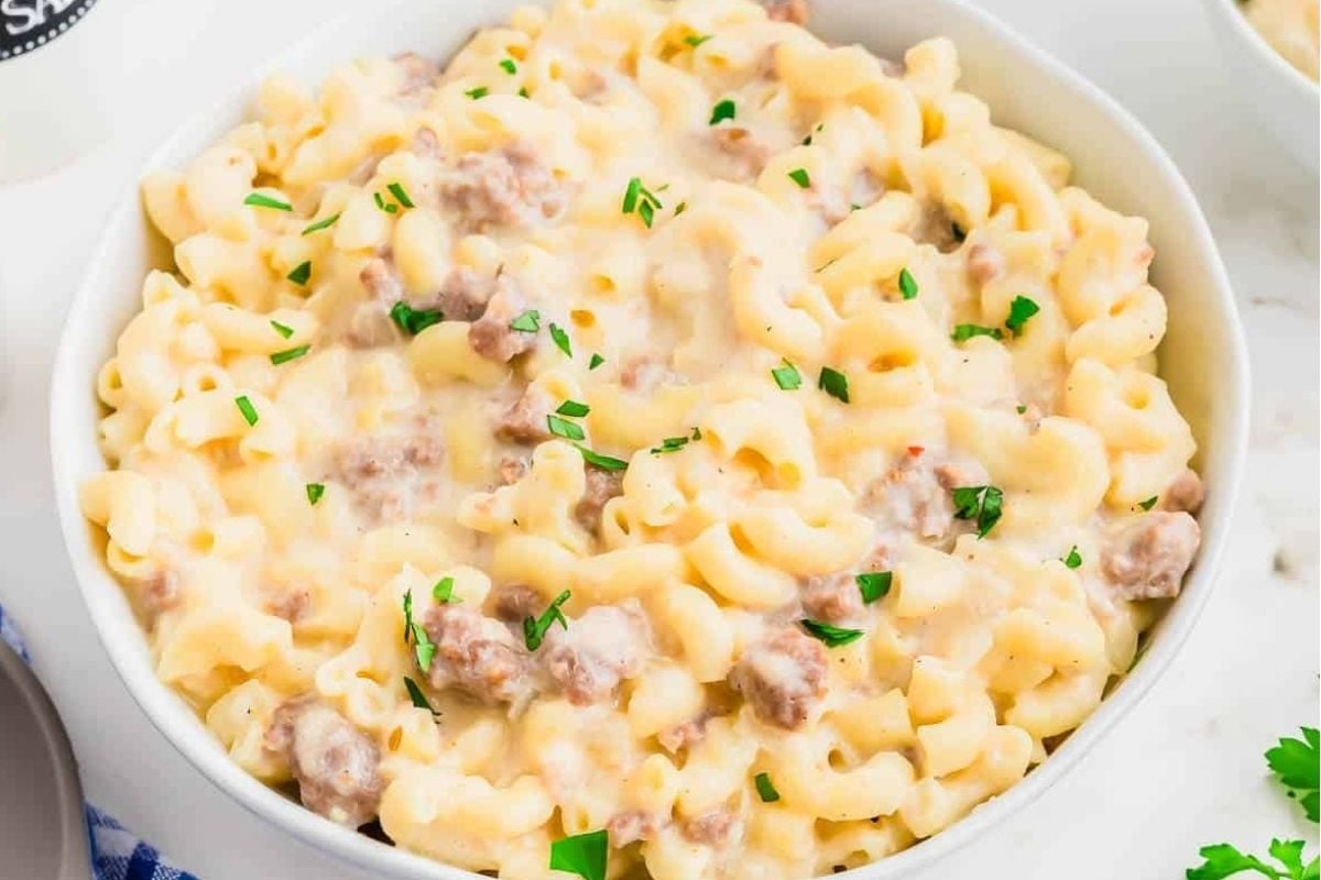 A bowl of creamy, cheesy macaroni and cheese with ground sausage and garnished with chopped parsley.