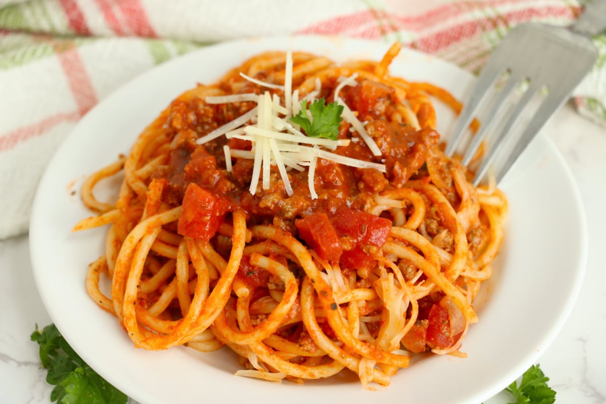 A plate of old school spaghetti with tomato sauce and sprinkled with shredded cheese.