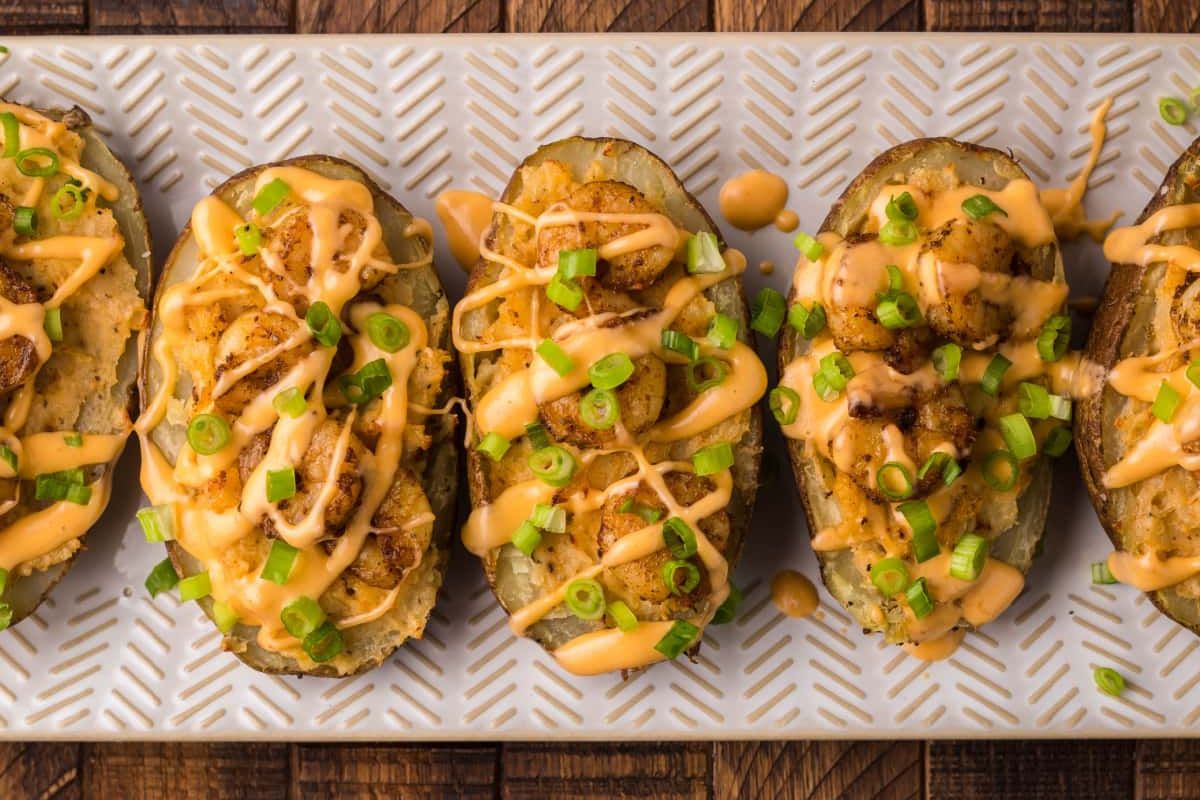Loaded baked potato skins topped with cheese sauce and green onions on a white serving platter, perfect for potato recipes enthusiasts.