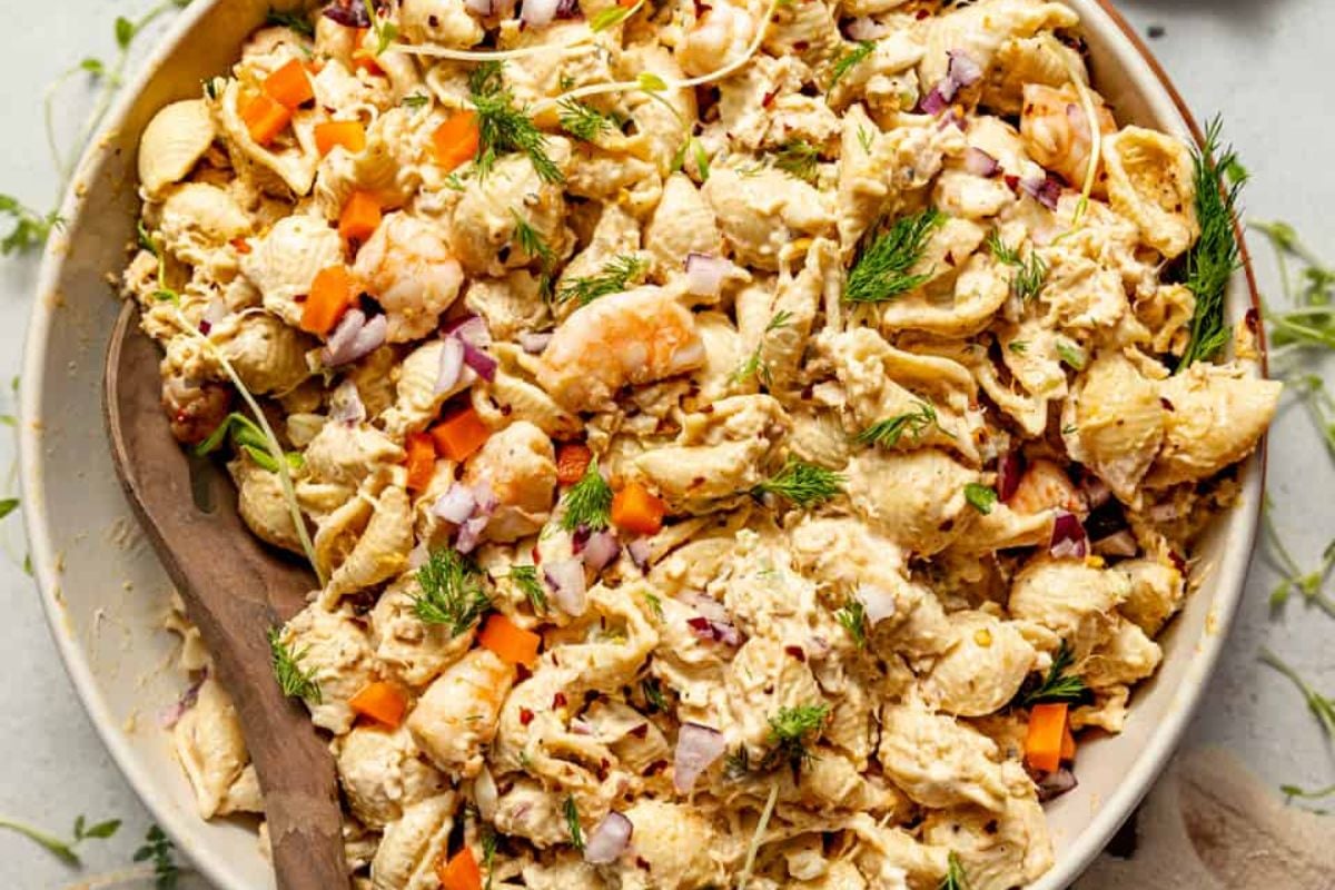 A bowl of seafood salad featuring shrimp, chunks of fish, diced carrots, red onions, and fresh dill on a light background&mdash;perfect for seafood recipes lovers.