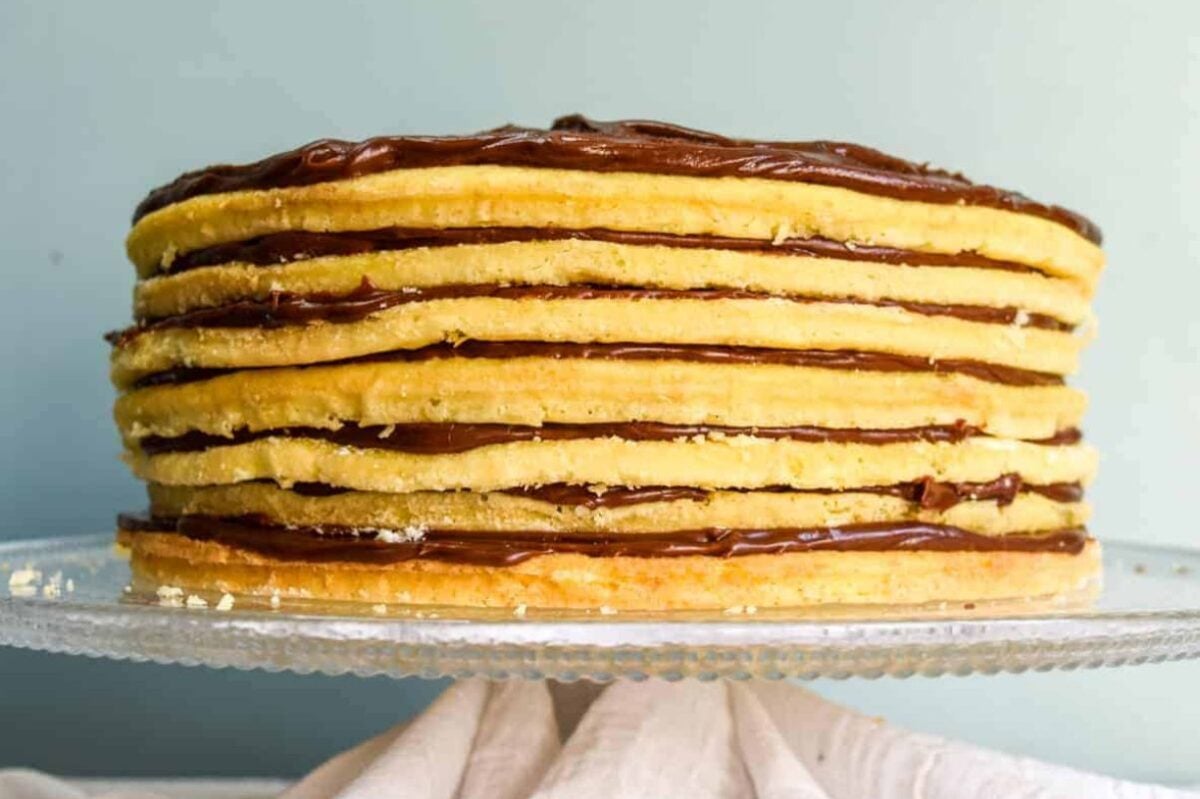 A stack of layer cakes with layers of chocolate spread on a glass serving plate.