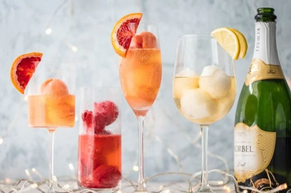 Various glasses of sorbet with fruit garnishes alongside a bottle of sparkling wine, perfect for Easter cocktails.
