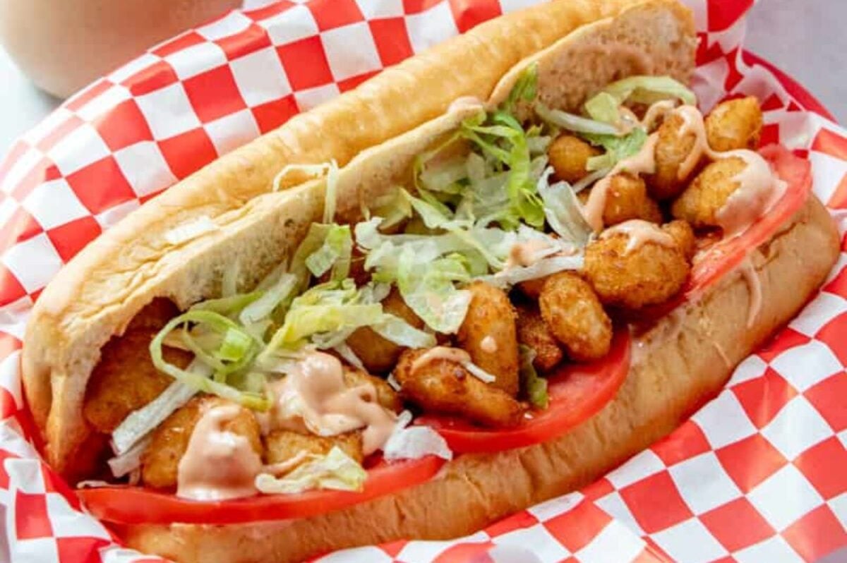 A po' boy sandwich filled with fried shrimp, lettuce, and sauce, served in a hoagie bun on a red and white checkered paper is a classic example of seafood recipes.