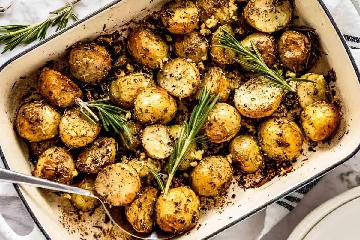 Potluck sides: Roasted potatoes in a baking dish with rosemary sprigs.