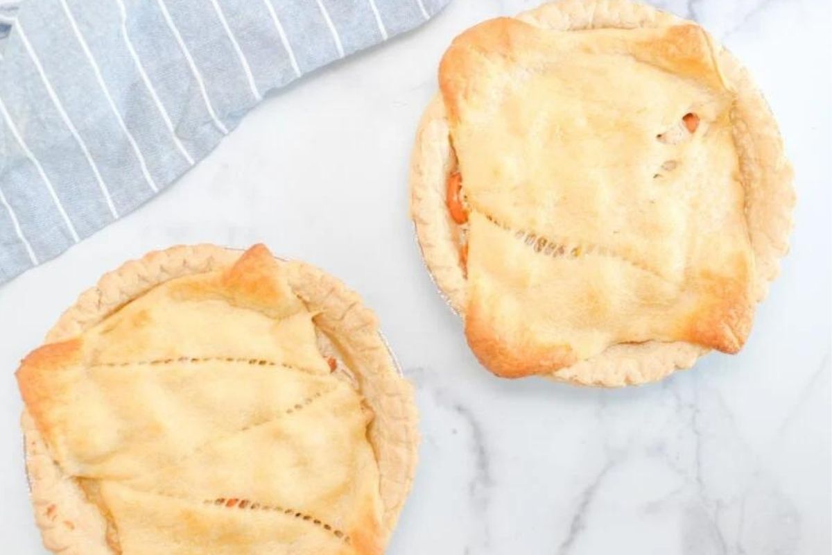 Two freshly baked, golden chicken pies on a marble countertop.