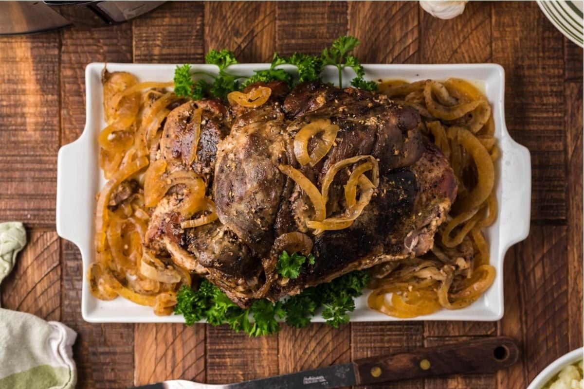 A large piece of meat with onions on a white plate from slow cooker recipes.