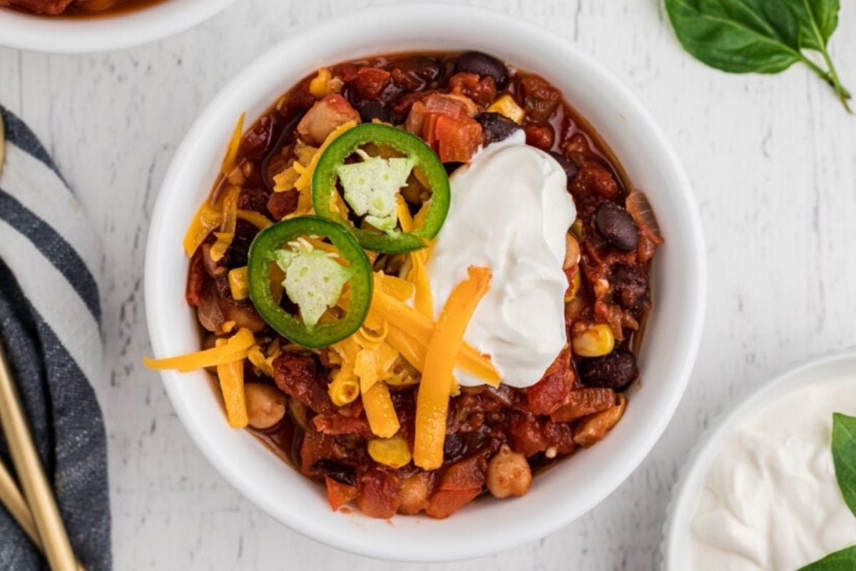 Bowl of chili topped with shredded cheese, sour cream, and sliced jalapeños on a white table—perfect for fans of comforting slow cooker recipes.