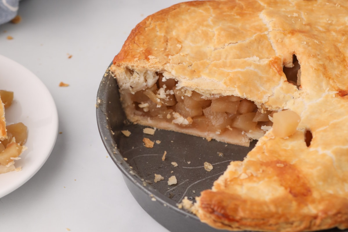 A freshly baked apple pie with a slice removed, revealing its filling, awaits to inspire your next culinary creation in our collection of pie recipes.