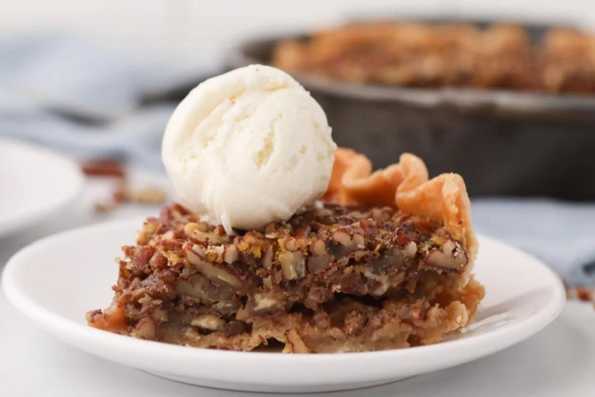 A slice of apple pie topped with a scoop of vanilla ice cream on a white plate, showcasing more pie recipes in the background.