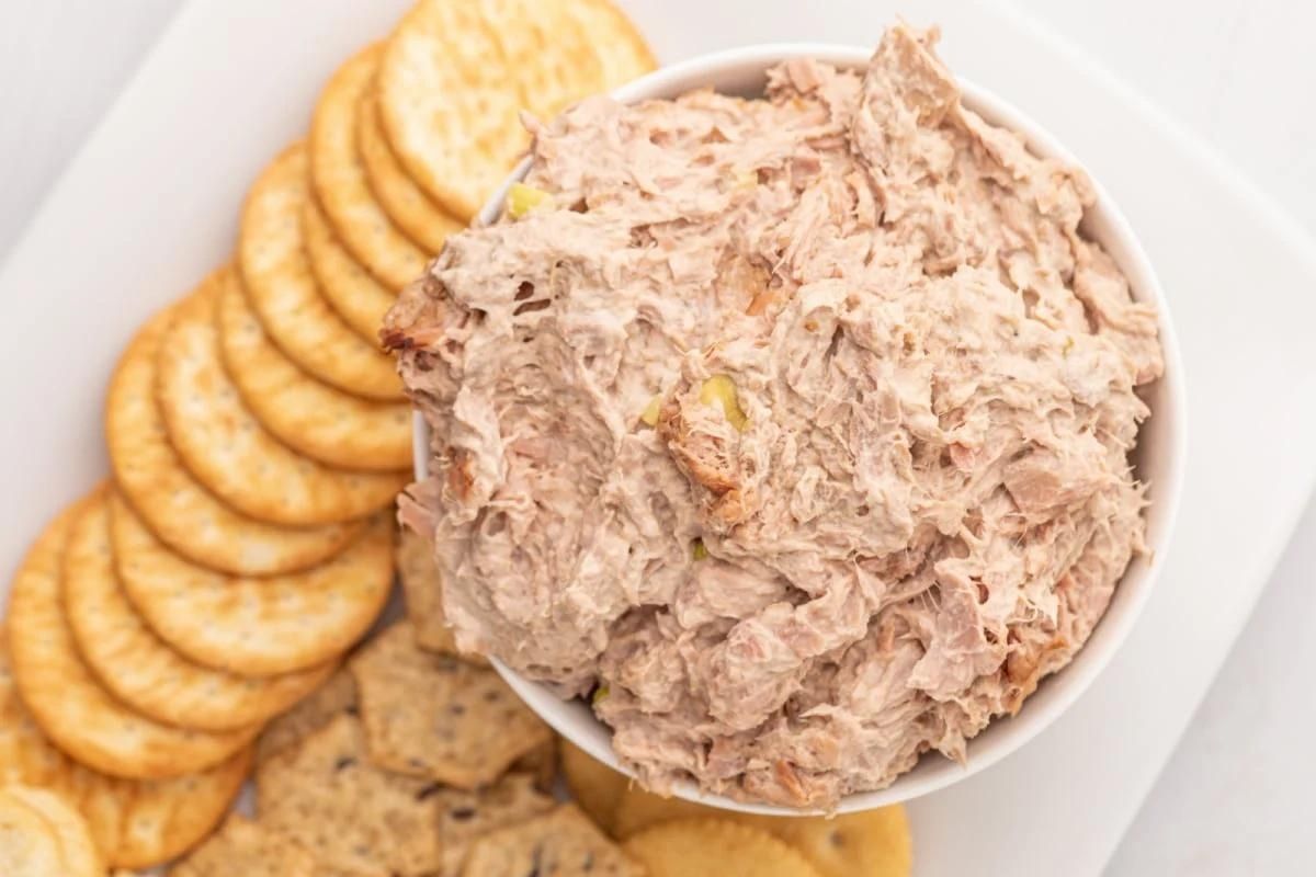 A bowl of tuna salad served with a selection of crackers and party dips.