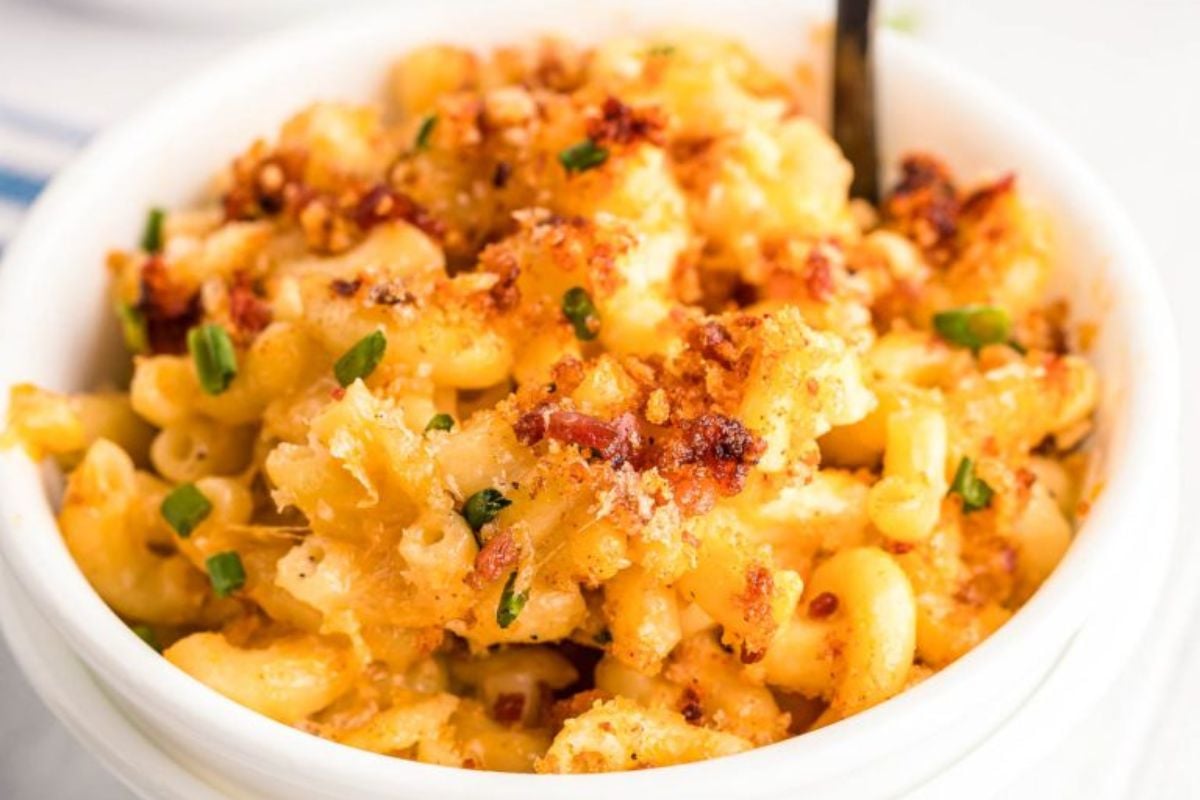 Creamy macaroni and cheese topped with crispy breadcrumbs and chives in a white bowl with a spoon—perfect for fans of classic cheesy recipes.