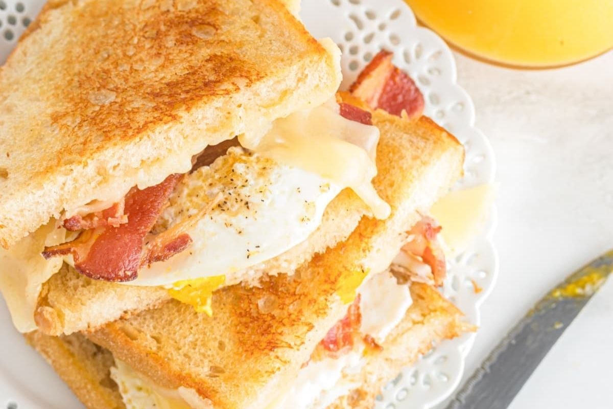 A close-up view of a Father's Day breakfast sandwich with bacon, egg, and melted cheese, served with a glass of orange juice on the side.