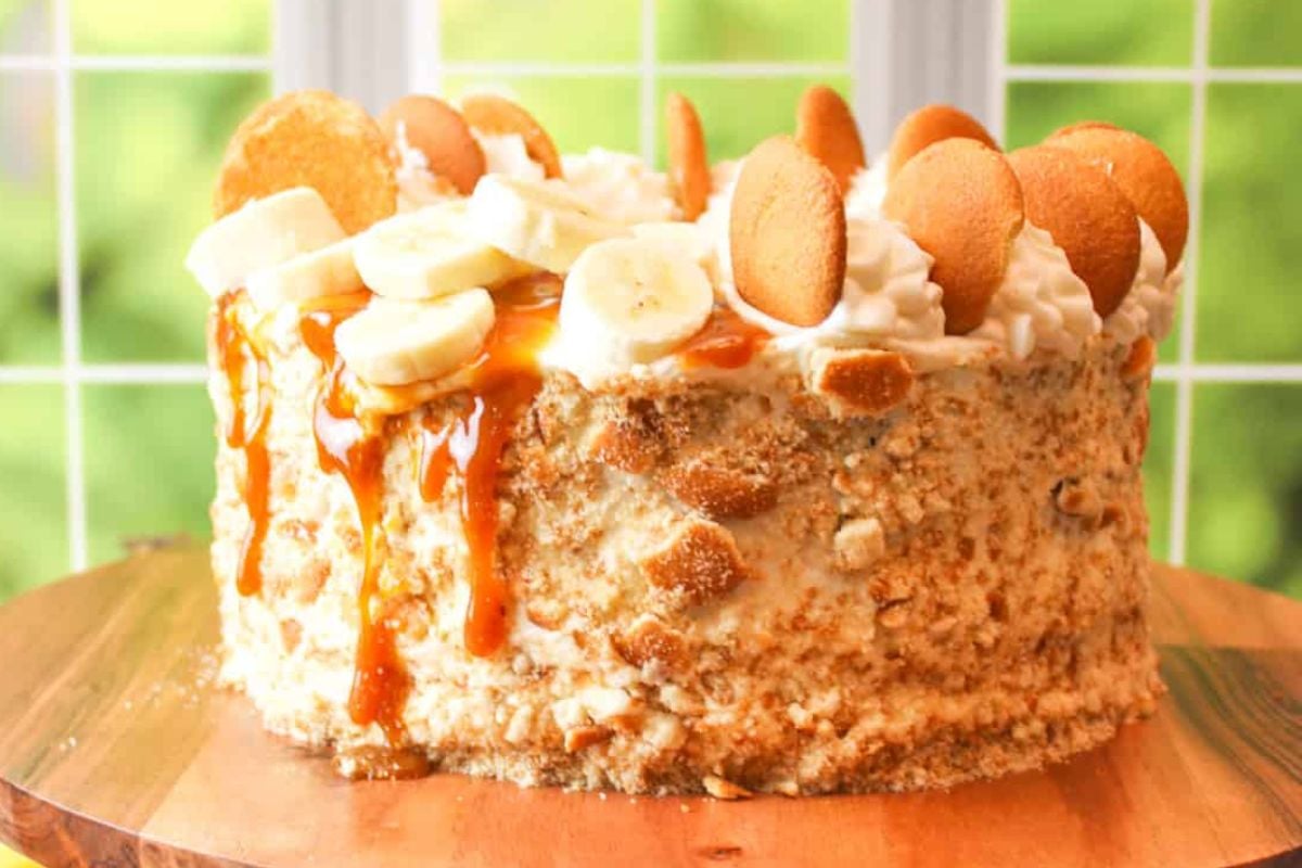 A banana pudding layer cake with vanilla wafers and banana slices on top, drizzled with caramel.