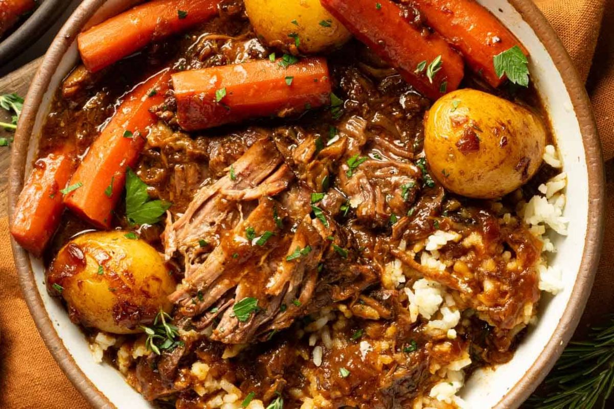 A hearty Easter dinner pot roast with carrots, potatoes, and garnished with herbs, served over a bed of rice.
