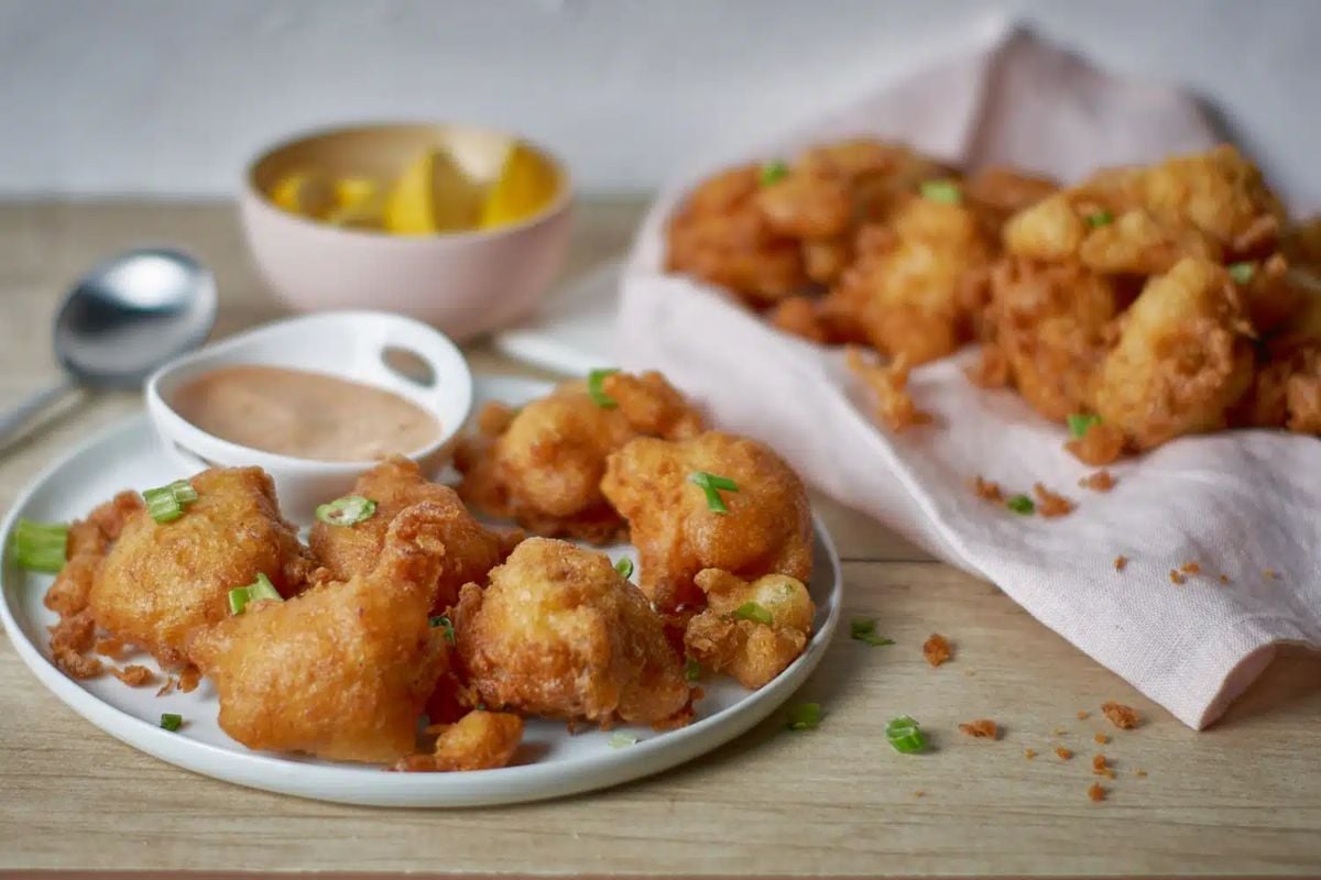 A plate of crispy fried shrimp from our seafood recipes, served with dipping sauces and lemon slices, garnished with chopped herbs on a wooden table.