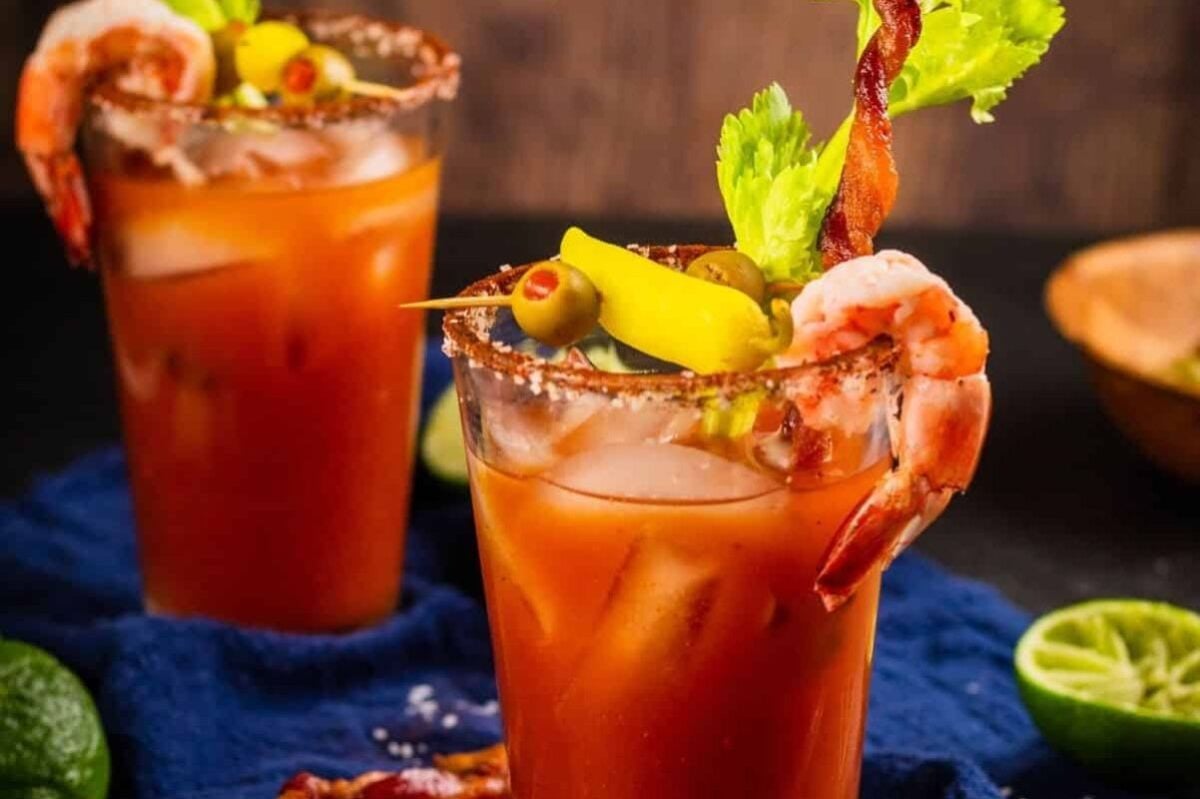 Two bloody mary Easter cocktails garnished with shrimp, celery, and olives.
