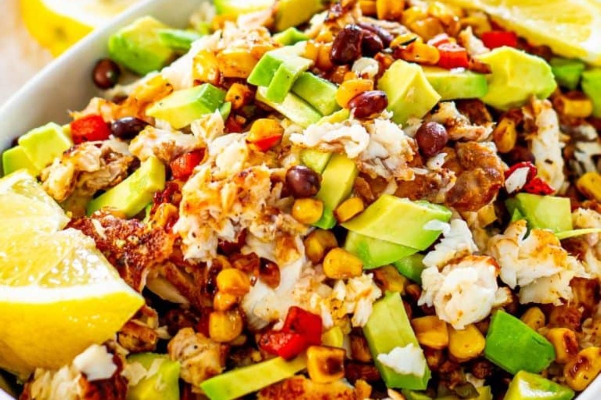 A colorful tex-mex salad with avocado, black beans, corn, and spiced seafood garnished with lime wedges.