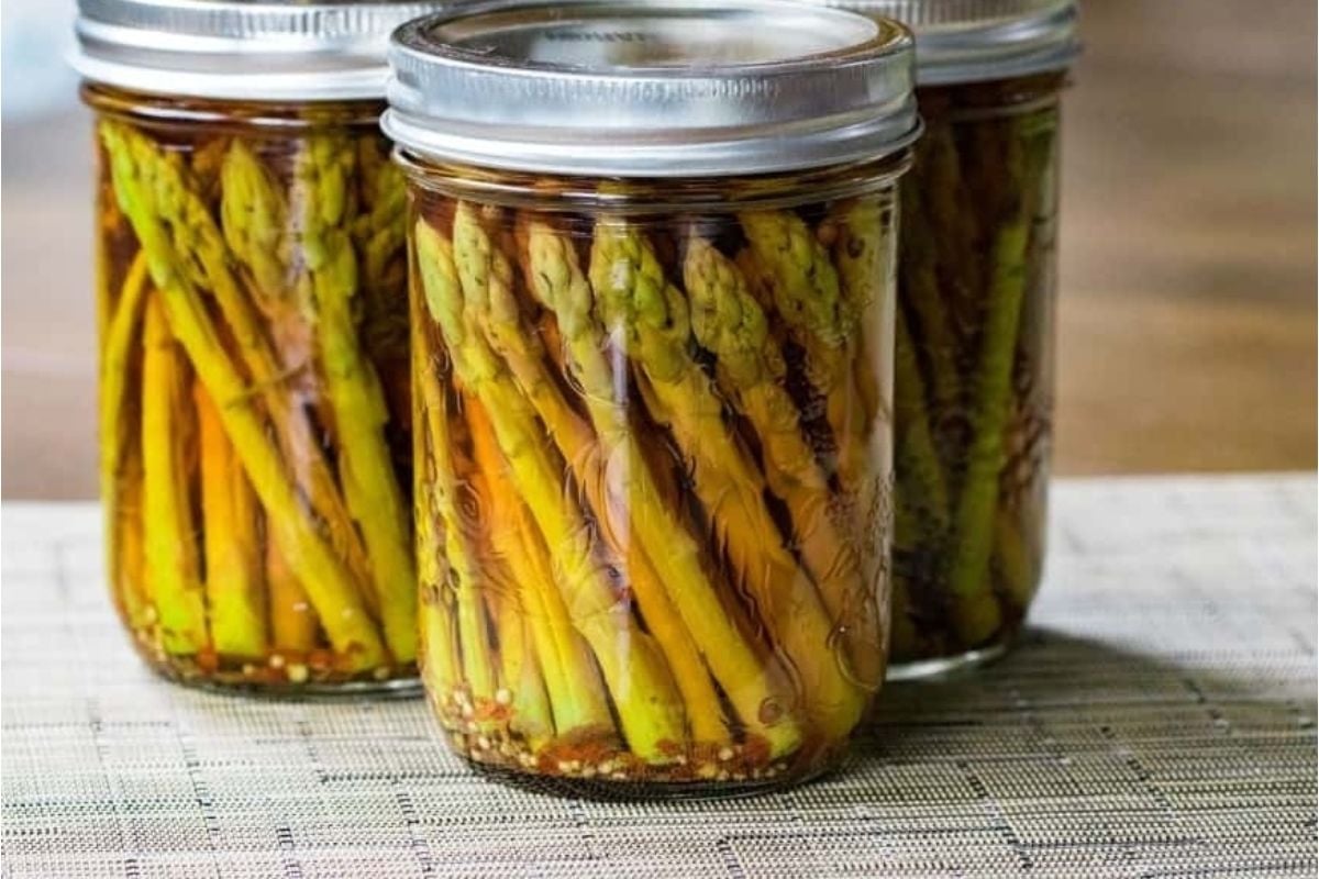 Jars of pickled asparagus featuring pickled recipes on a textured surface.