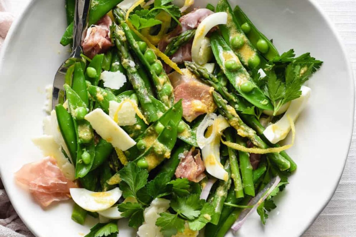 A plate of green asparagus salad with hard-boiled eggs and ham slices, perfect for Easter sides.