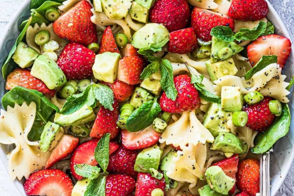 A bowl of pasta salad with strawberries, avocado, and mint, perfect for potluck sides.