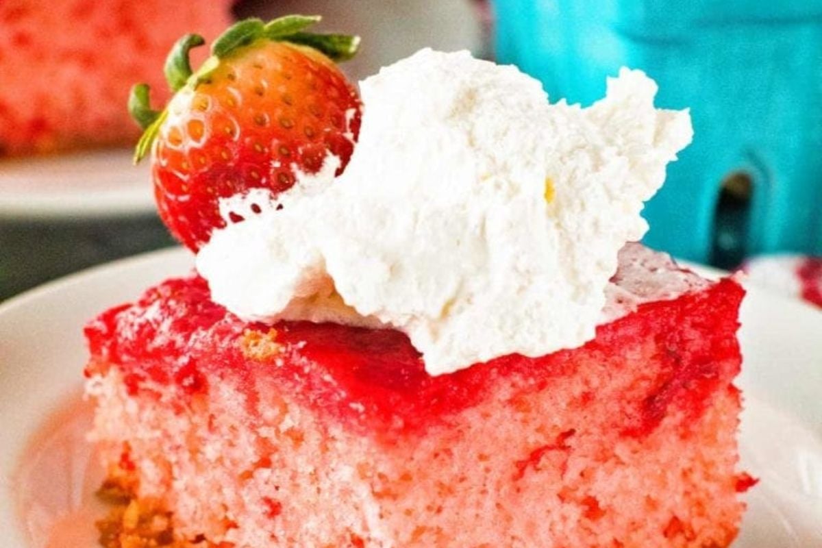 A slice of strawberry cake, inspired by classic upside down cakes, topped with whipped cream and a fresh strawberry on a white plate.