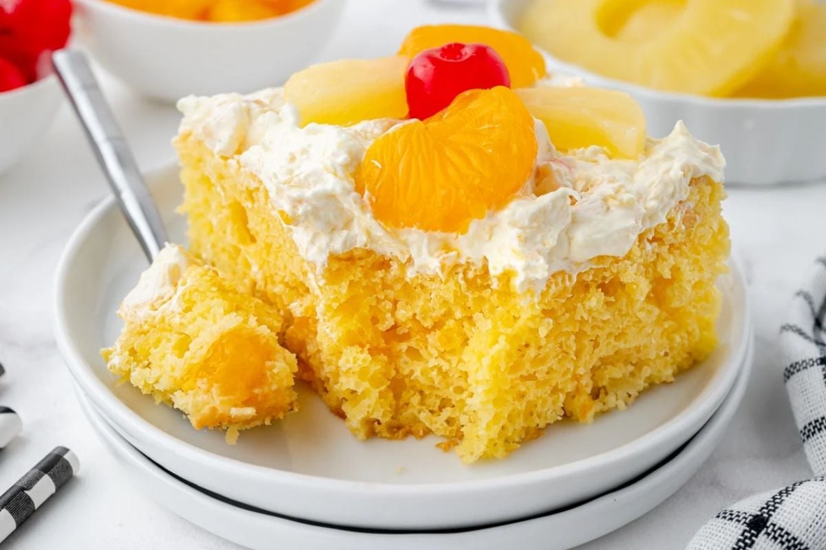 A slice of pineapple upside-down Easter cake topped with whipped cream and garnished with a cherry on a white plate.