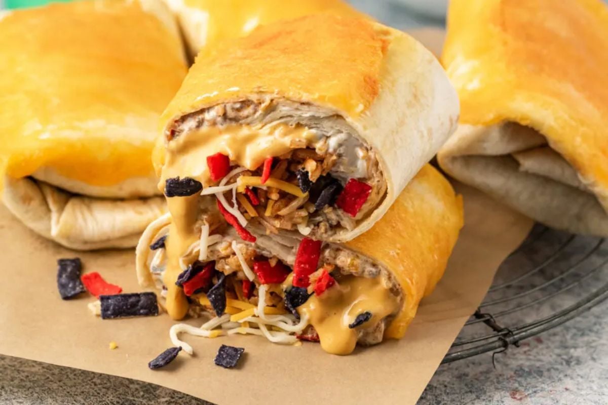 Stuffed burrito recipes with melted cheese, black beans, and diced red peppers on parchment paper.