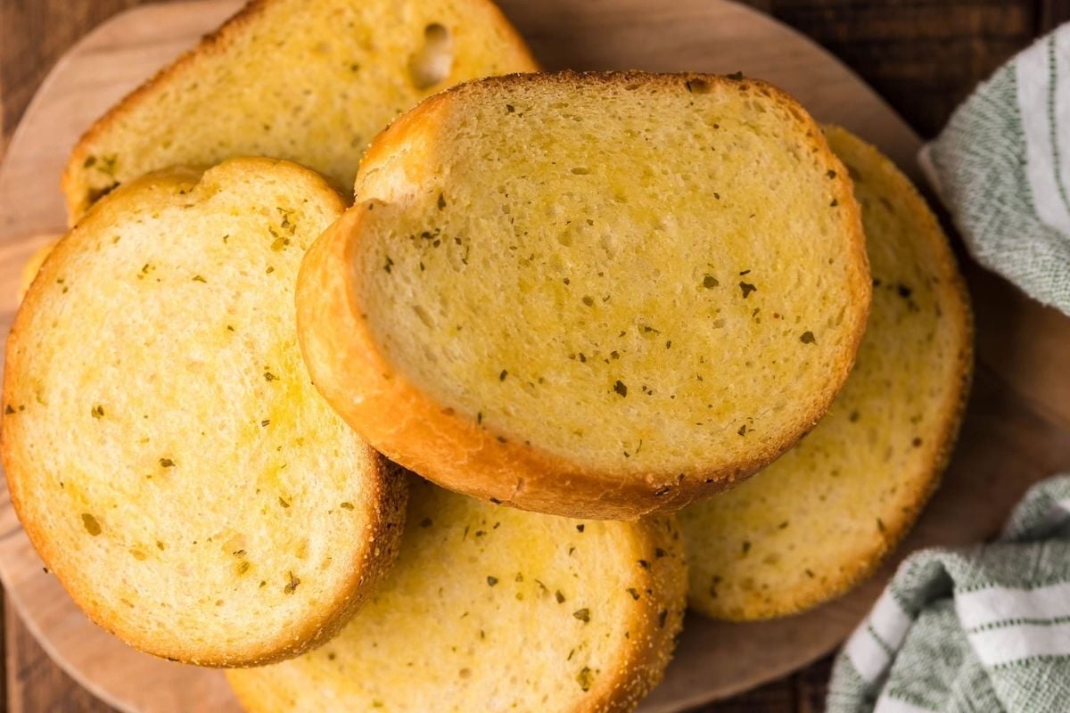 Slices of garlic bread arranged on a wooden serving board for an air fryer breakfast.