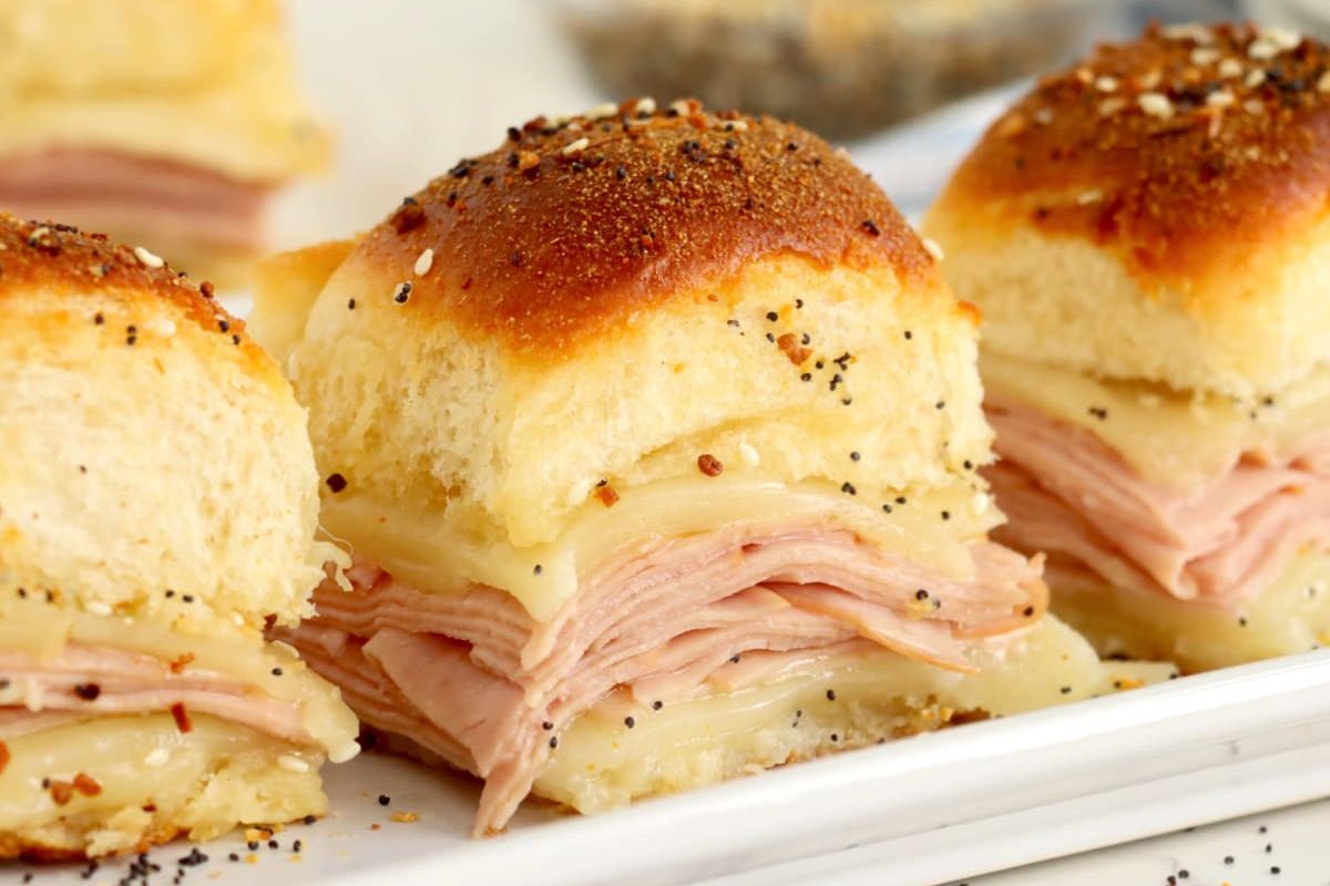 Freshly baked sliders with ham and melted cheese, topped with sesame seeds, perfect for an Easter appetizer.