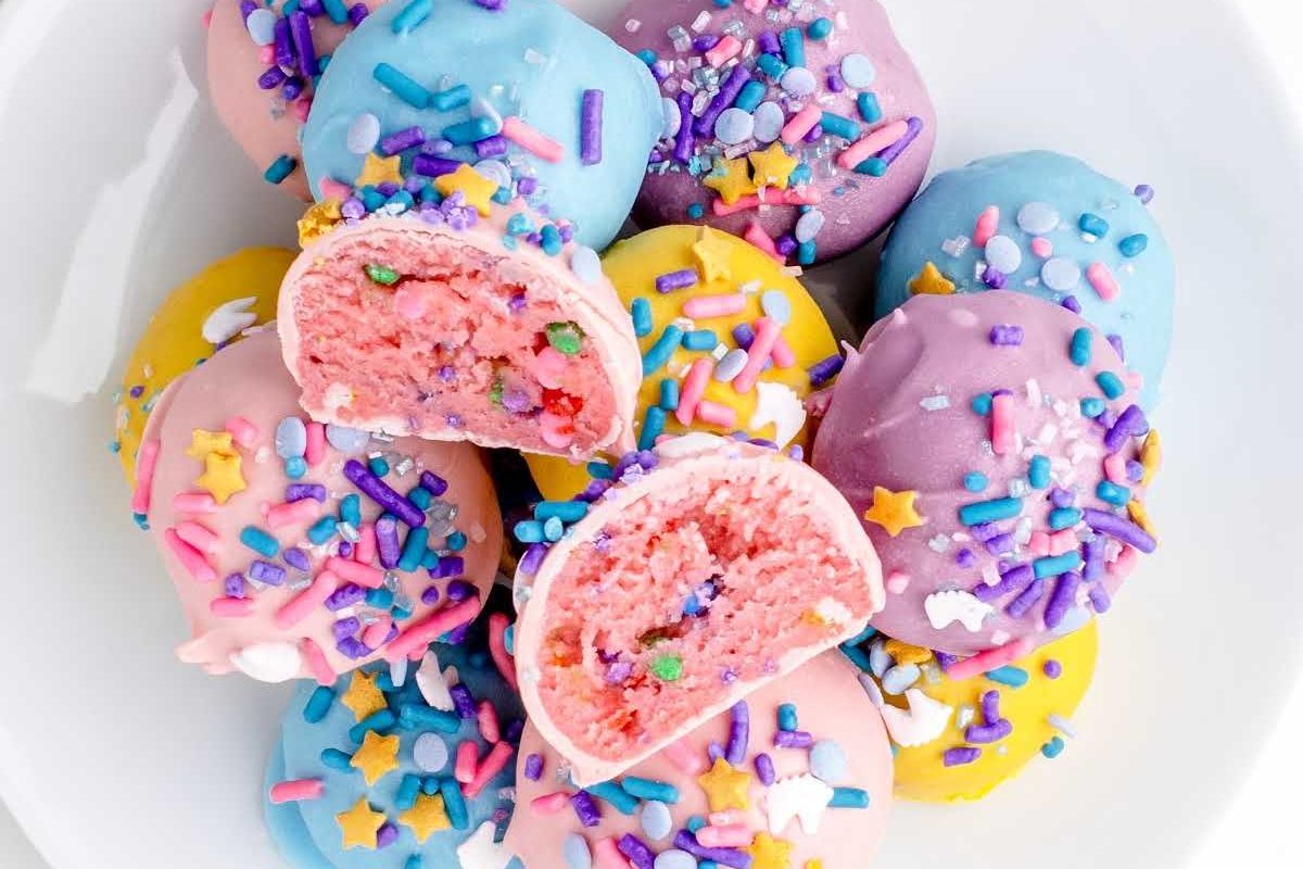 Plate of colorful Easter dessert cake pops with one cut in half to reveal pink cake inside, adorned with sprinkles.