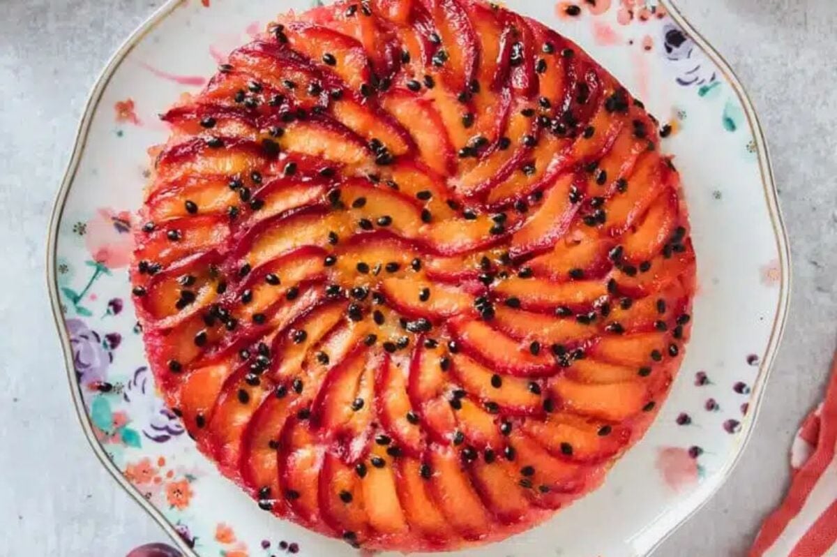 A round upside-down cake topped with neatly arranged plum slices and sprinkled with passion fruit seeds—a delightful twist on classic upside down cakes.