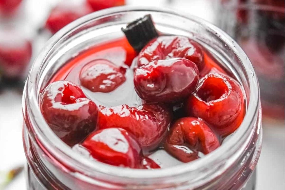 Jar of preserved cherries on a white surface, perfect for pickled recipes.