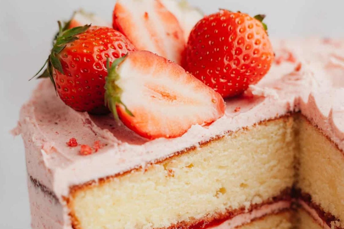 A close-up of a slice of layered strawberry cake garnished with whole and sliced strawberries.